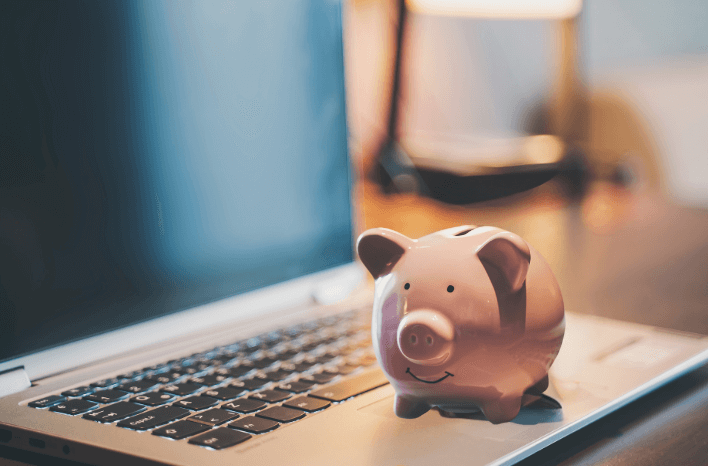A piggy bank sits on top of a laptop computer. Blog post on ways schools can maximize digital marketing with a limited budget