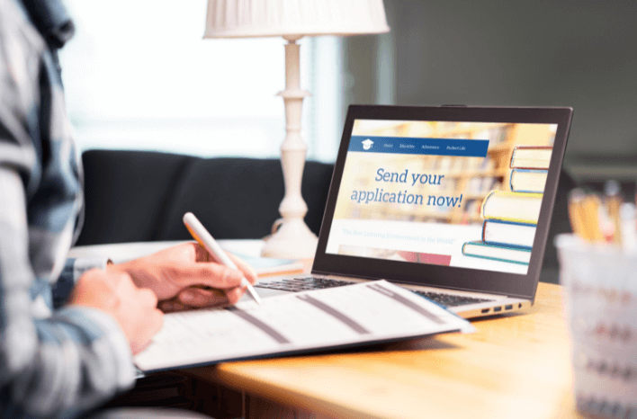 parent filling in application form with computer, pen and paper | school admissions is changing as parents do ample research ahead of time | Truth Tree is a leading digital marketing agency working exclusively with school and education companies