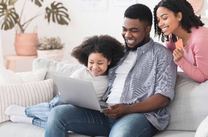 a family smiles at lap top screen presumedly looking at school options | image accompanies blog post on the power of strong school branding for awareness and recognition | truth tree school marketing blog post