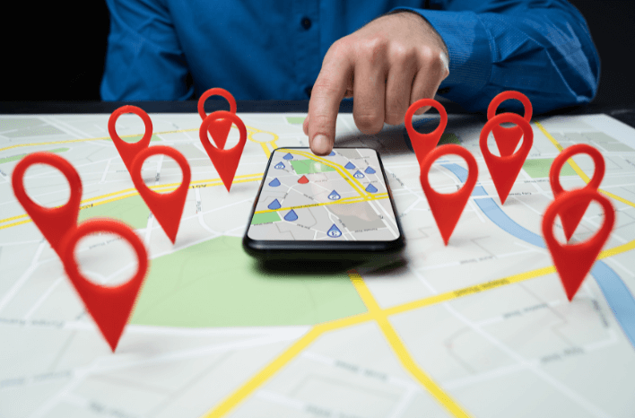 Map with location markers hovering above it with a mobile phone sitting in the center with a hand hovering just above it | image accompanies a blog post by Truth Tree on geofencing as a school marketing tactic