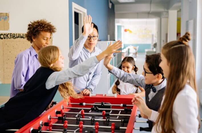 Students and teacher enjoying a foosball game together. | Accompanies a blog post by Truth Tree on feeder school marketing.